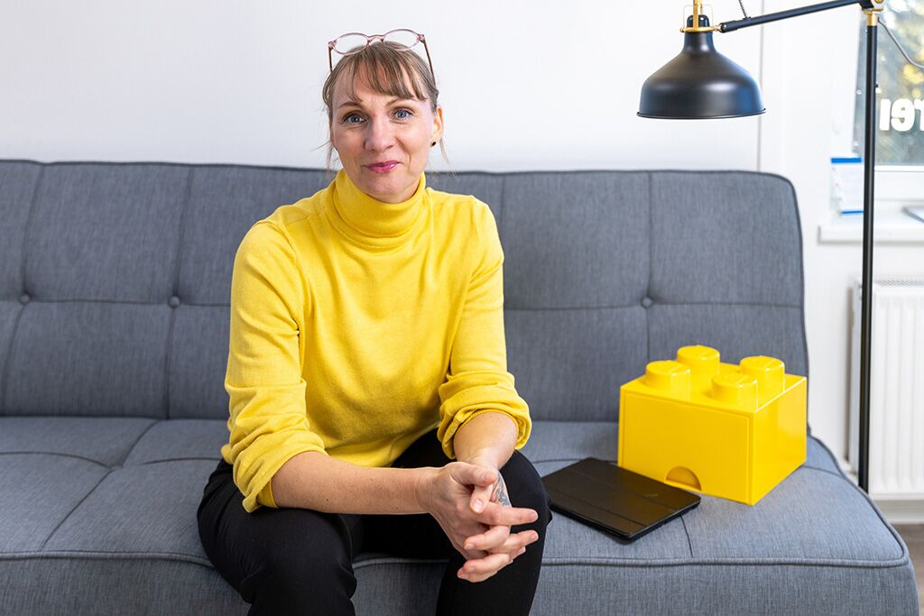 Maren Thier, Expertin für Markenstrategien und ganzheitliche Kommunikationskonzepte in gelbem Pullover sitzt auf grauer Couch