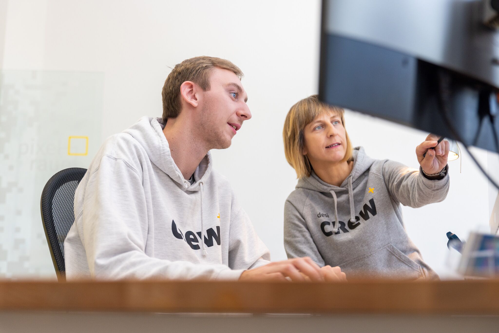 Webdesign: zwei Mitarbeiter in desi-Hoodies besprechen sich am Rechner