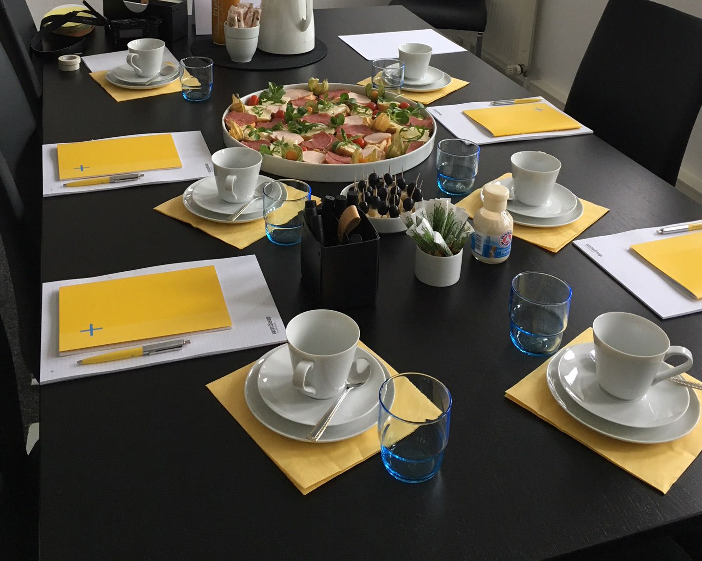 Fertig für den Strategieworkshop! Blick auf den vorbereiteten Sitzungstisch mit Arbeitsmaterialien, Kaffeetassen, Gläsern und Imbiss.