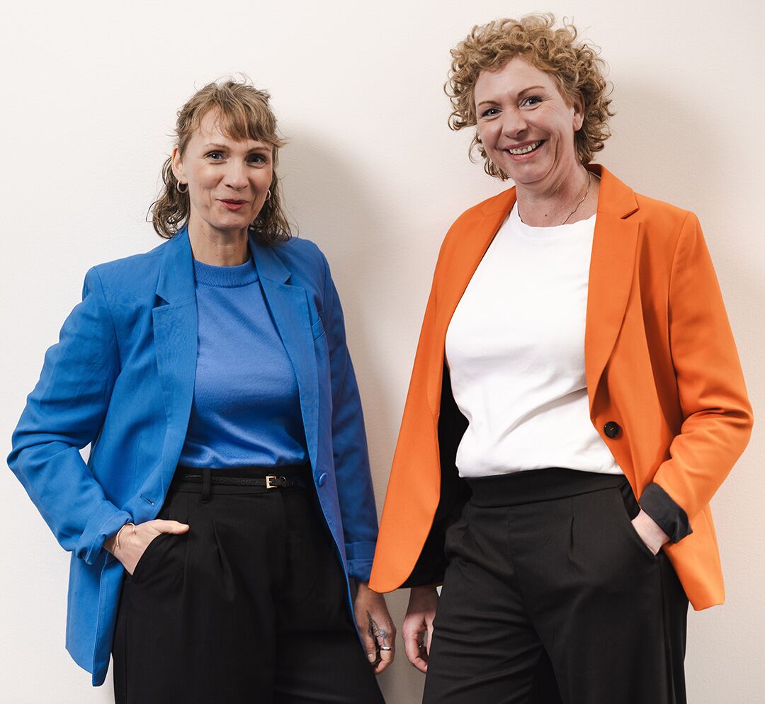 im Halbporträt lächelnd an weißer Wand lehnend: Maren Thier und Anja Eglmeyer als Ansprechpartner für Markenstrategien