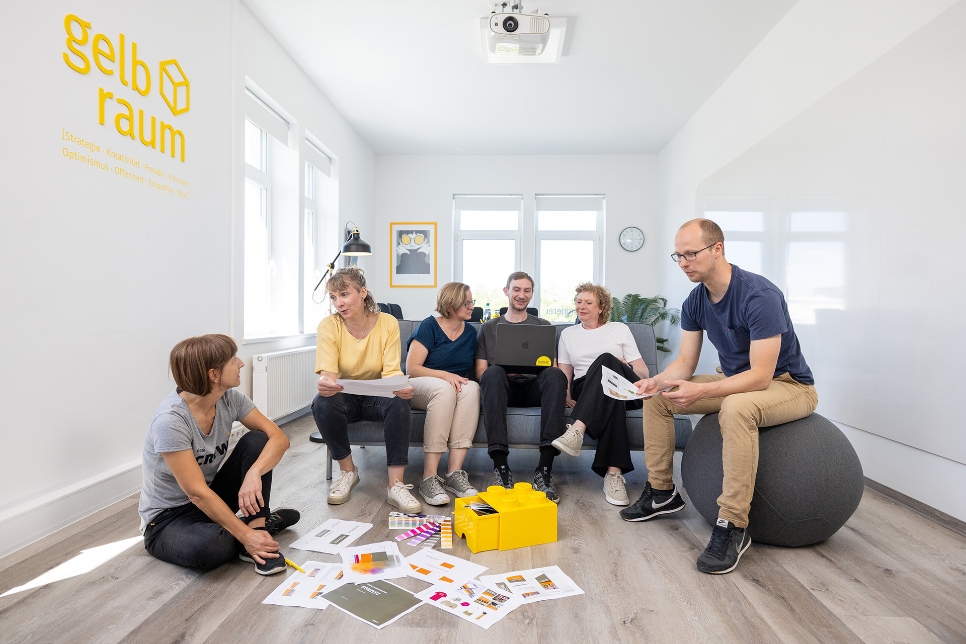 designerei-Team im gelbraum, versammelt um Entwürfe, besprechen Strategisches Design